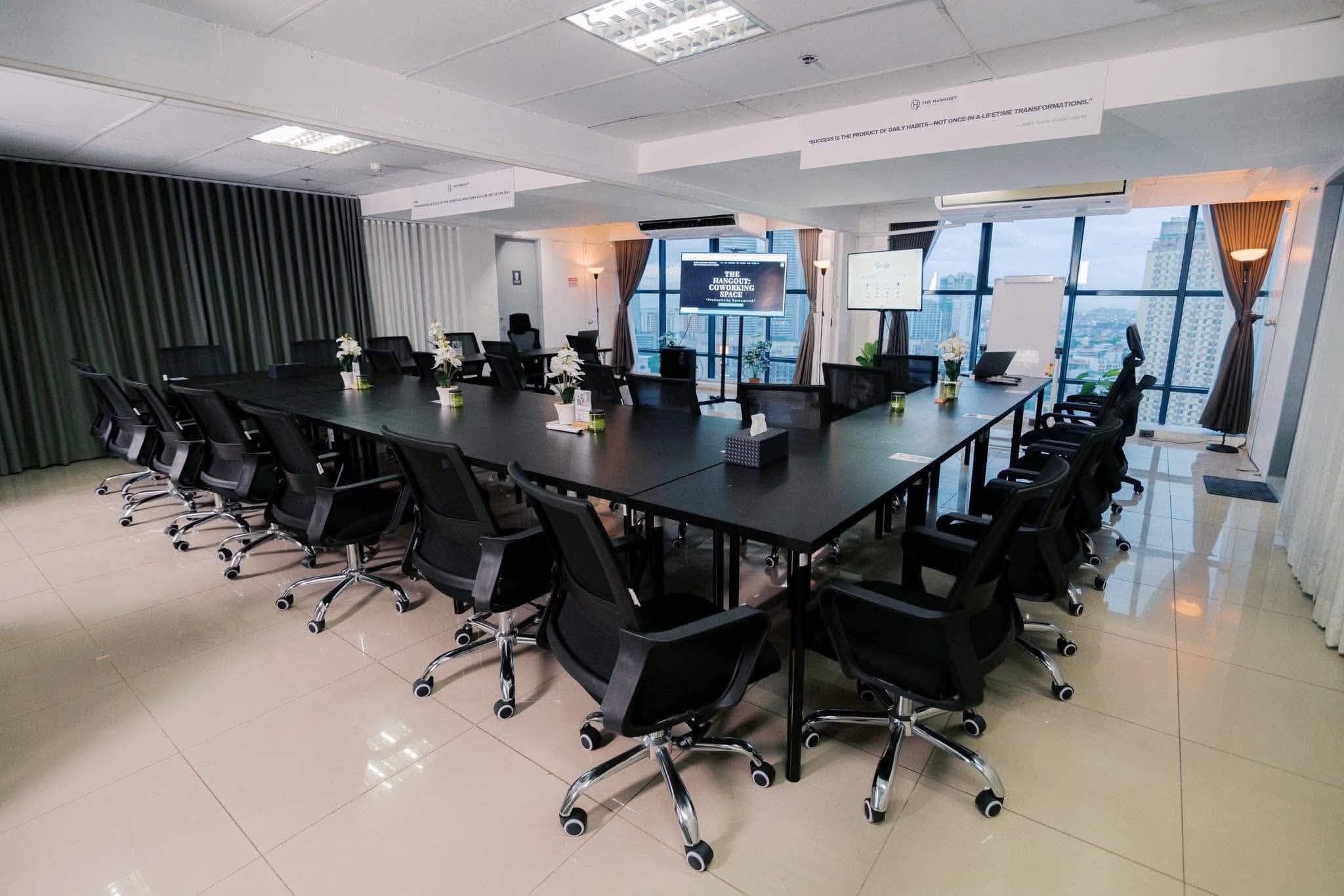 Classroom setup at The Hangout Coworking Space — boardroom-style tables, presentation screens, and floor-to-ceiling city windows